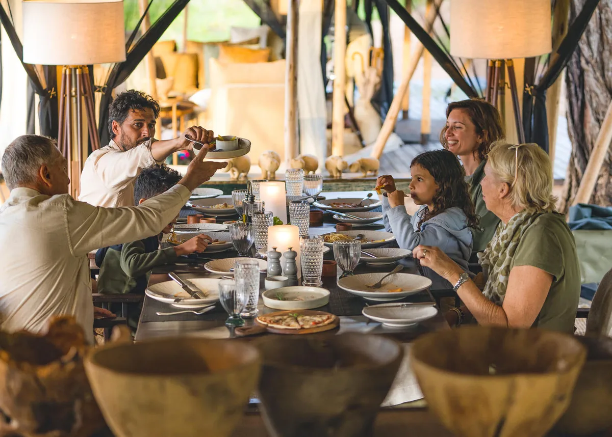 Three generations of a family passing dishes around a long table in the mess tent