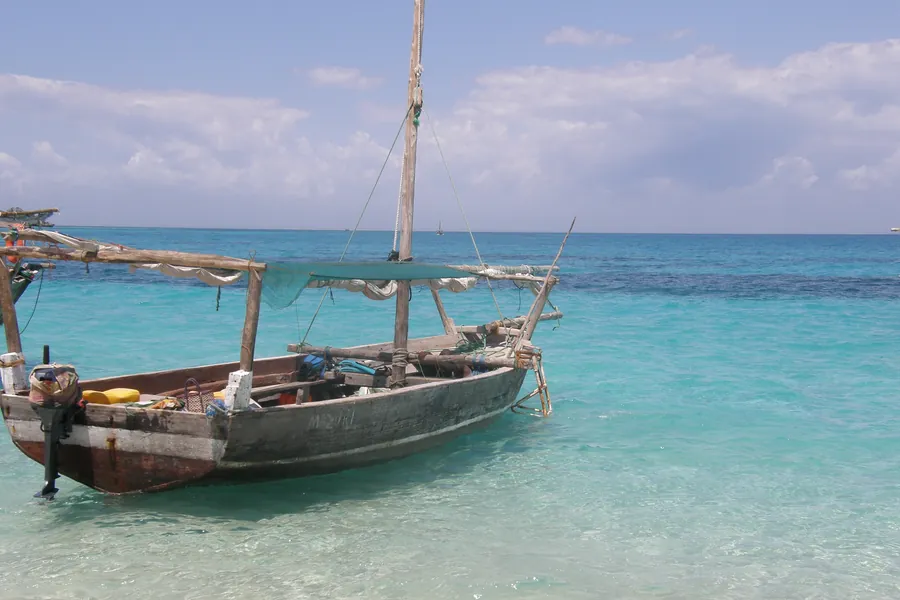 A traditional wooden outrigger boat moored in clear turquoise shallows near Kwale Island off Zanzibar