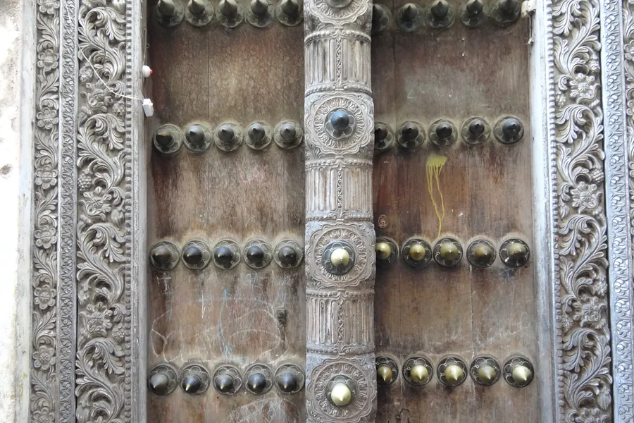 A close-up of a carved wooden Zanzibar door in Stone Town, with ornate floral frames and rows of brass studs