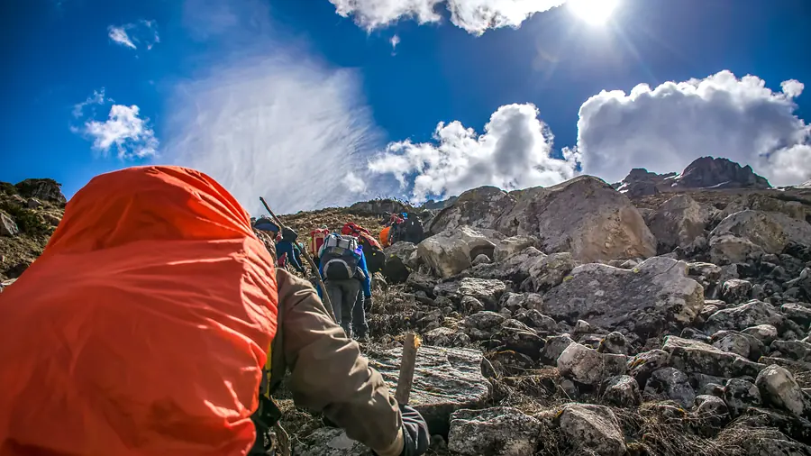 Trekkers picking a way between pale boulders with towering cloud building over the ridge above